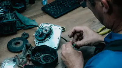 An adult male technician repairing a mechanical gear system on a wooden table indoors.