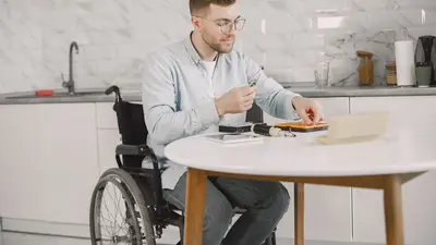 Man in wheelchair fixing electronics on a table in a modern kitchen setting.