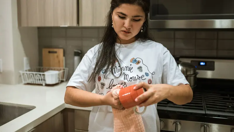 Woman in a white shirt cleaning a red mug in a modern kitchen setting.