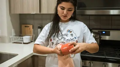 Woman in a white shirt cleaning a red mug in a modern kitchen setting.