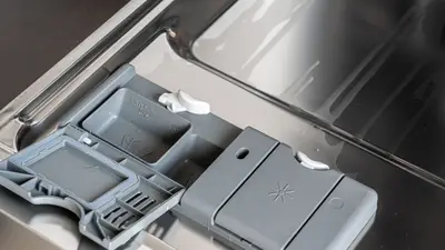 A detailed view of a dishwasher detergent compartment with soap residue.