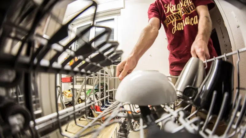 POV perspective of an adult loading dishes into a dishwasher in a home kitchen.
