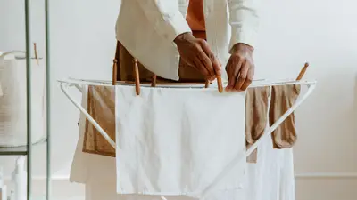 A man uses wooden clips to hang laundry indoors, emphasizing household routines and care.