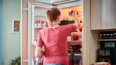 A woman opens the fridge to retrieve food items in a cozy kitchen setting.