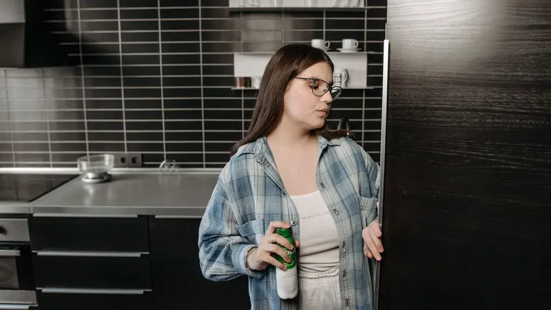 A woman holding a drink opens the refrigerator in a sleek, modern kitchen.