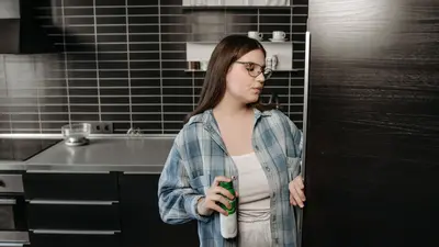 A woman holding a drink opens the refrigerator in a sleek, modern kitchen.