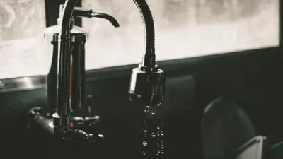 Close-up of a kitchen faucet with water droplets falling into the sink, captured in a minimalist style.