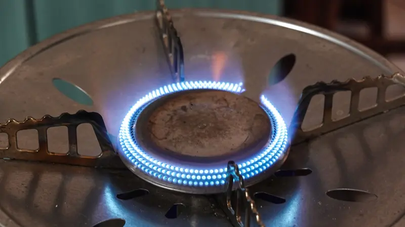 A detailed view of a lit gas stove burner with visible blue flames and metal support.