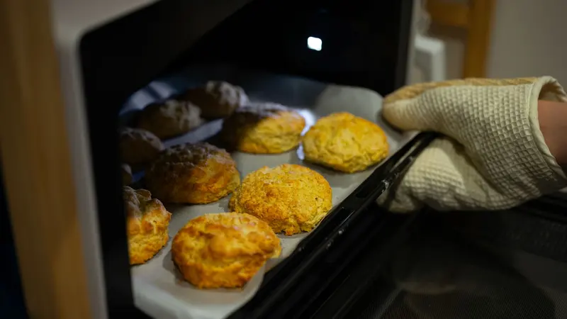 A warm, inviting scene of fresh biscuits being taken out of the oven with an oven mitt.