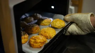 A warm, inviting scene of fresh biscuits being taken out of the oven with an oven mitt.
