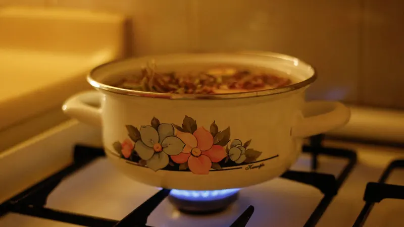 A floral design enamel pot on a gas stove with simmering soup, creating a warm kitchen ambiance.
