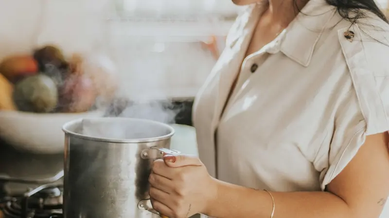 A woman boiling water in a stainless steel pot on a stove, creating a cozy kitchen atmosphere.