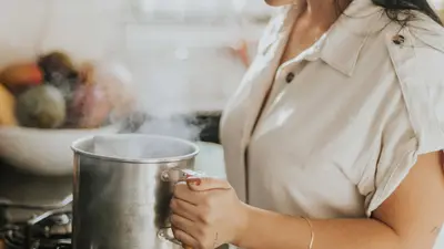 A woman boiling water in a stainless steel pot on a stove, creating a cozy kitchen atmosphere.