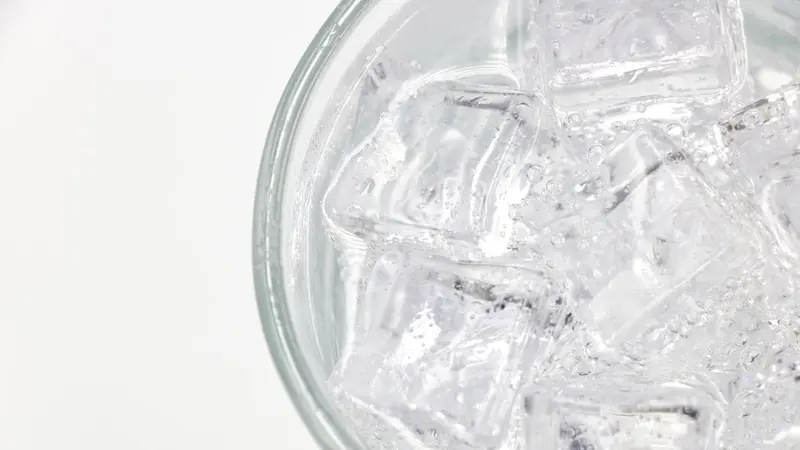 Close-up of a glass filled with sparkling water and ice cubes on a white background.