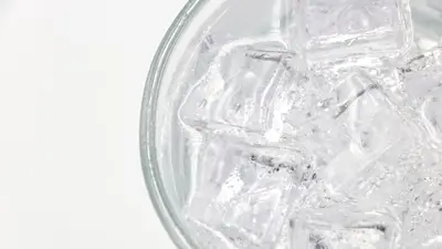 Close-up of a glass filled with sparkling water and ice cubes on a white background.