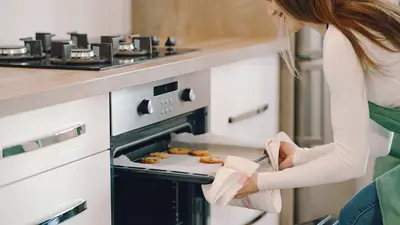 A woman pulls freshly baked cookies from an oven in a modern kitchen setting.
