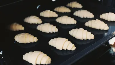 Close-up of uncooked croissants on a baking tray in an oven, captured indoors.
