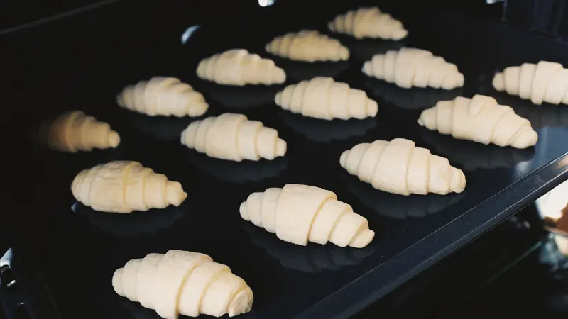 Close-up of uncooked croissants on a baking tray in an oven, captured indoors.