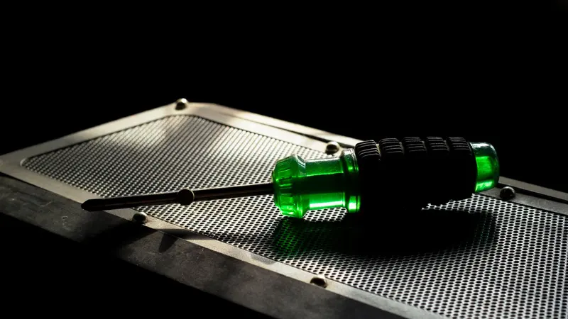 A green screwdriver with a black grip resting on a metallic perforated surface in a studio setting.
