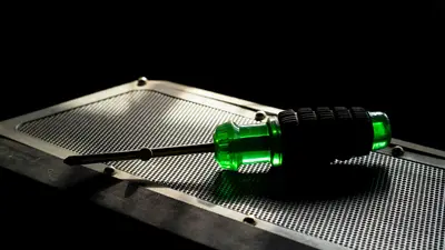 A green screwdriver with a black grip resting on a metallic perforated surface in a studio setting.