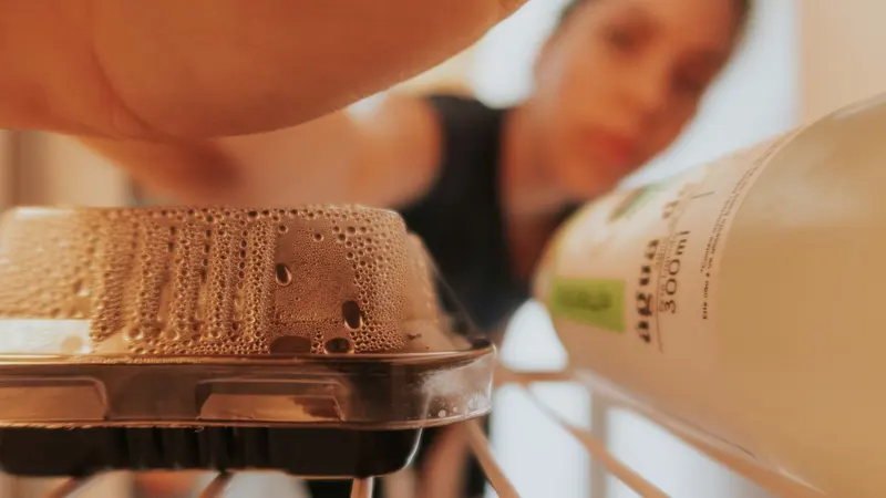 Blurred woman reaching into refrigerator, focusing on food container and drink bottle.