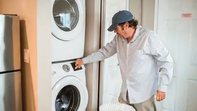 A man places clothes in a washing machine at home, focusing on household chores.