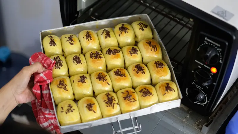 A tray of freshly baked buns being taken out of a home oven.