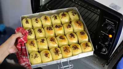 A tray of freshly baked buns being taken out of a home oven.