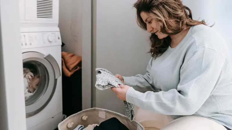 Woman organizing laundry in a laundry room with a washing machine.