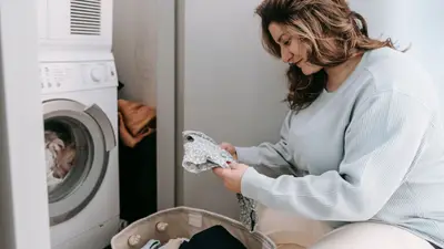 Woman organizing laundry in a laundry room with a washing machine.