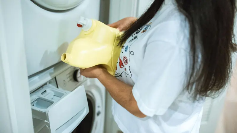 A woman pours detergent into a washing machine for a laundry cycle.