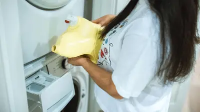 A woman pours detergent into a washing machine for a laundry cycle.