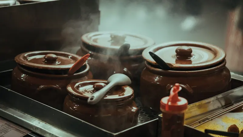 Close-up of steaming traditional clay pots with utensils on a stove, creating a cozy kitchen ambiance.