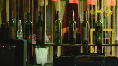 A row of green wine bottles and a Corona bottle on a wooden shelf indoors.